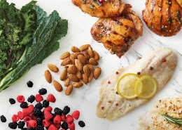 Cooked fish with lemon slices, berries, nuts, greens, grains, and chicken breast