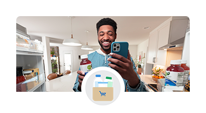 A smiling man holding a nutritious drink, making a nutrition appointment on his phone right from his kitchen. 
