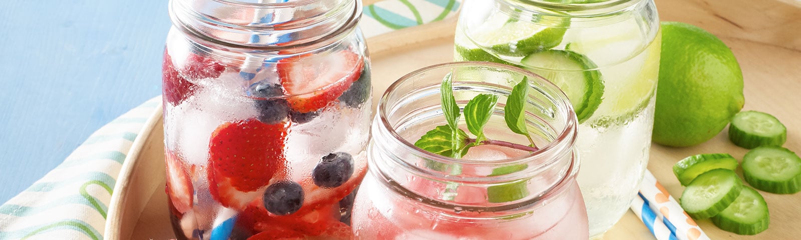 Mason jars filled with water, ice cubes and berries sitting on a tray