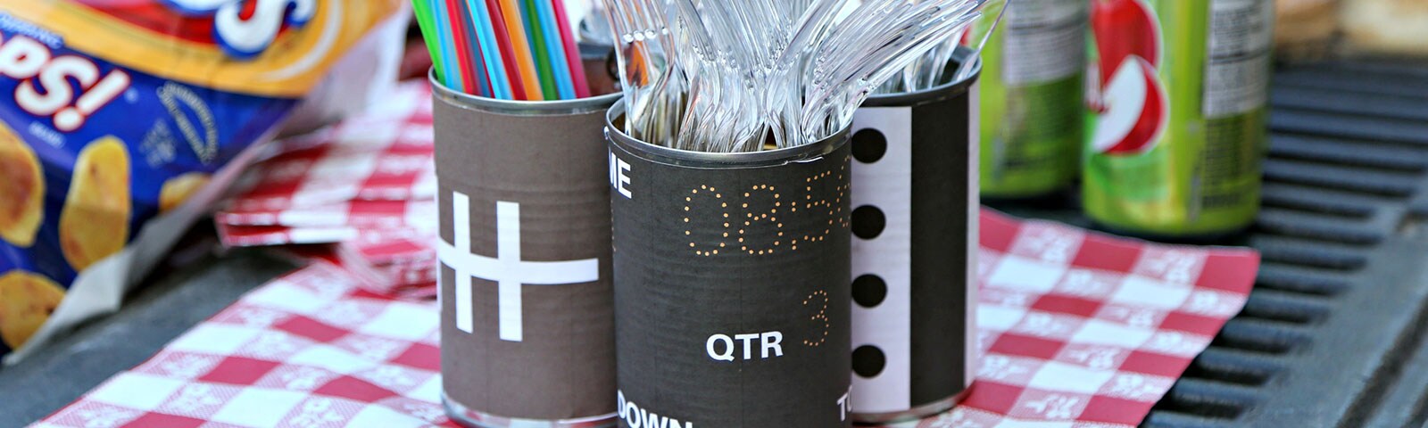 Plastic silverware and colorful straws in tin can decorated as footballs