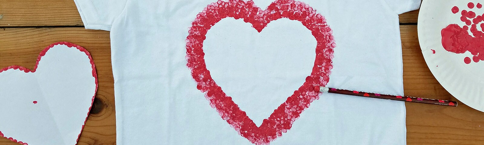 White t-shirt laid flat on the floor with a DIY stamped red outline of a heart in the middle
