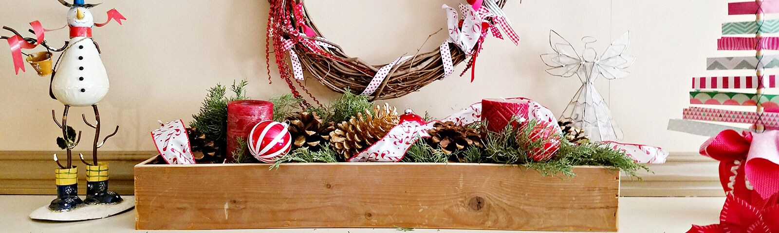  A wooden box on a mantle filled with evergreen clippings, ornaments, garland and festive candles