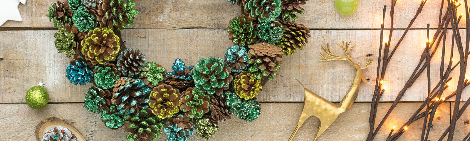 A large pinecone wreath dusted in glitter of various colors sitting on a rustic wooden table