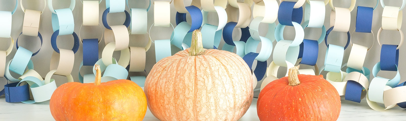 Three pumpkins sitting in front of a background of paper chains in various color papers hanging from above
